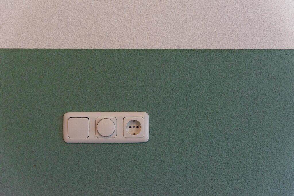 Close-up of a power outlet and switch on a textured green wall indoors.