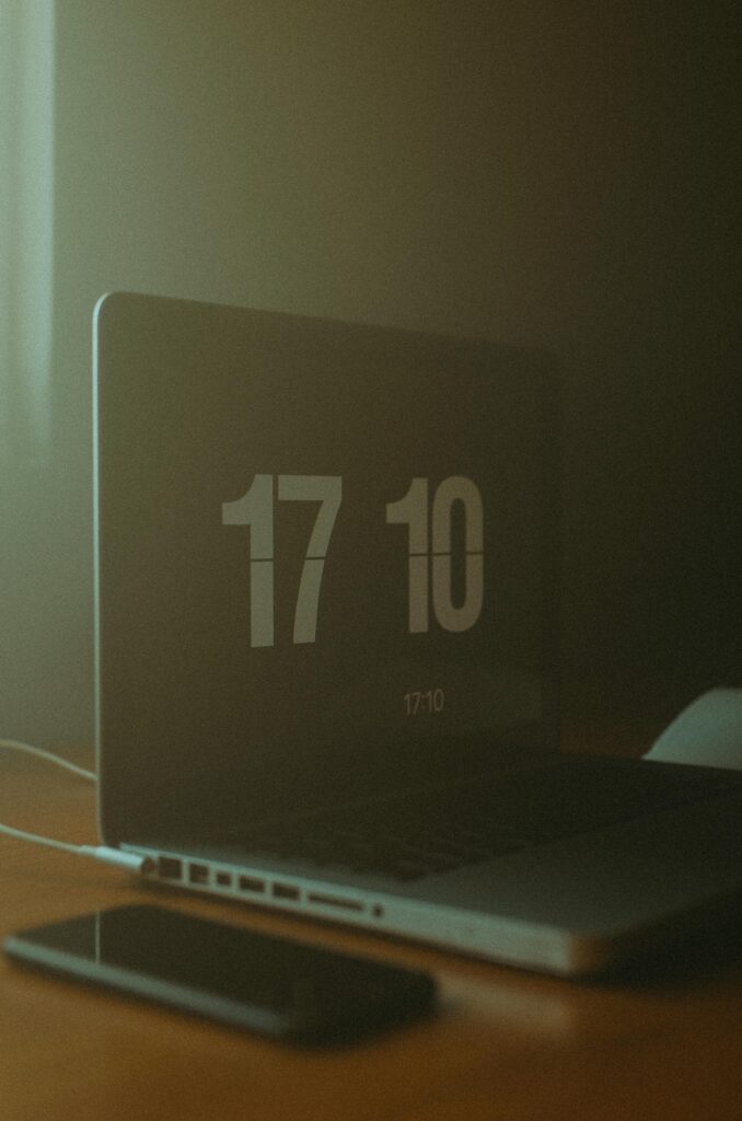 A dimly lit workspace featuring a laptop displaying the time and a smartphone on the table.